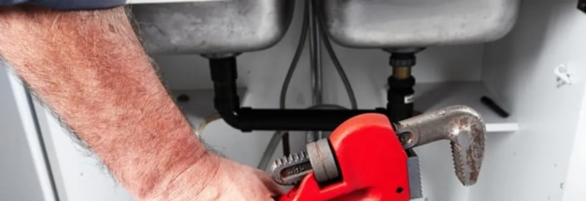 Garbage disposal repair technician tightening drain connections under a kitchen sink in Dallas, TX