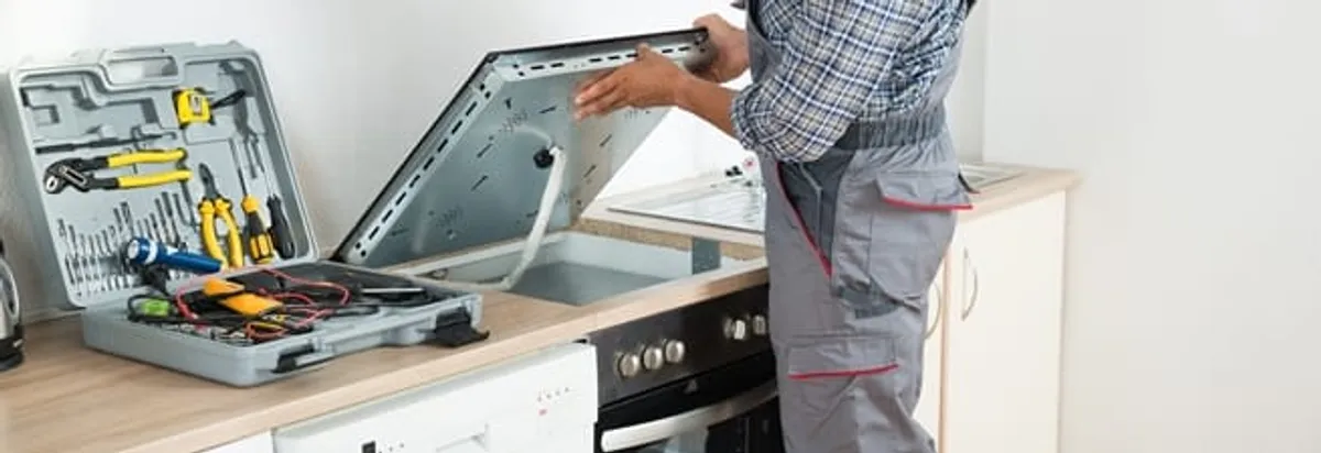 Cooktop repair technician lifting a built-in stovetop for service in Dallas, TX