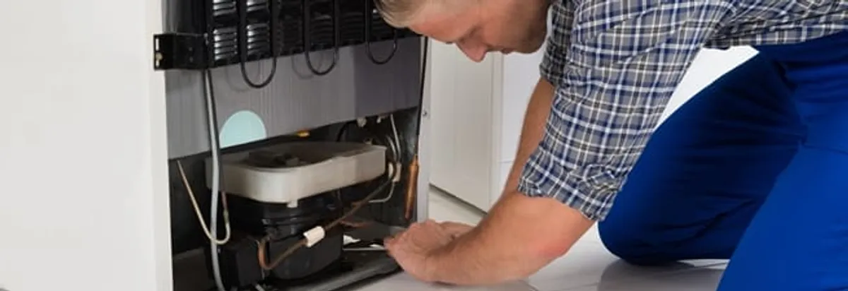 Refrigerator repair technician servicing the compressor and condenser area in Dallas, TX
